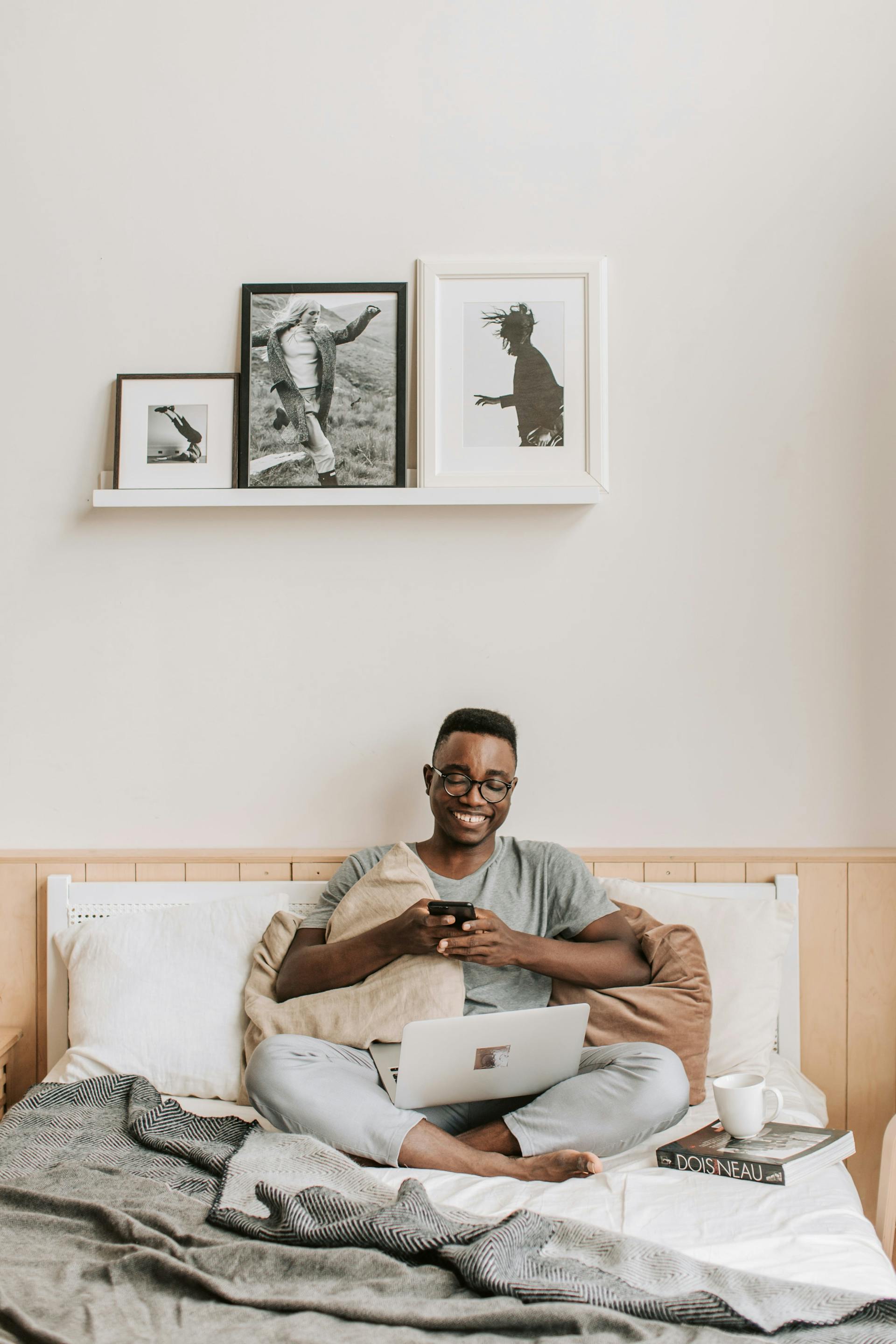 A man sitting on a bed smiling and texting