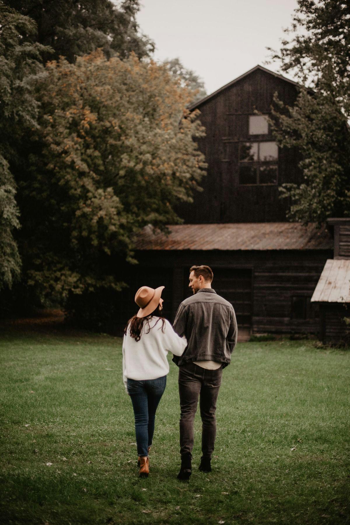 A male and female couple arm in arm walking toward a stylish barn in the forest